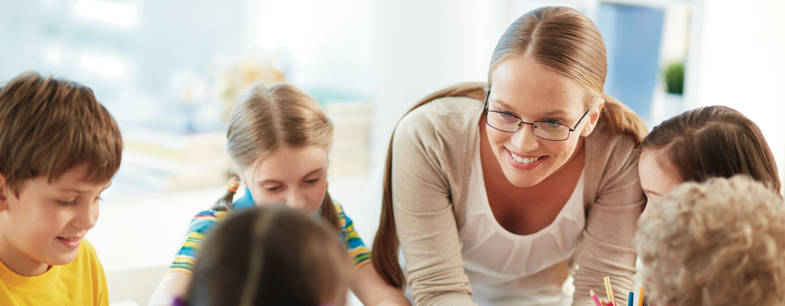 Childcare educator engaging with a small group of young children in a bright early learning centre, sitting together on the floor during a structured activity. The space features child-sized furniture, educational resources and a welcoming indoor environment, reflecting quality early childhood education and care in Victoria.