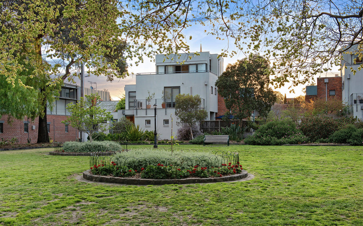 Landscaped communal garden with mature trees, flowering garden beds and open green space.