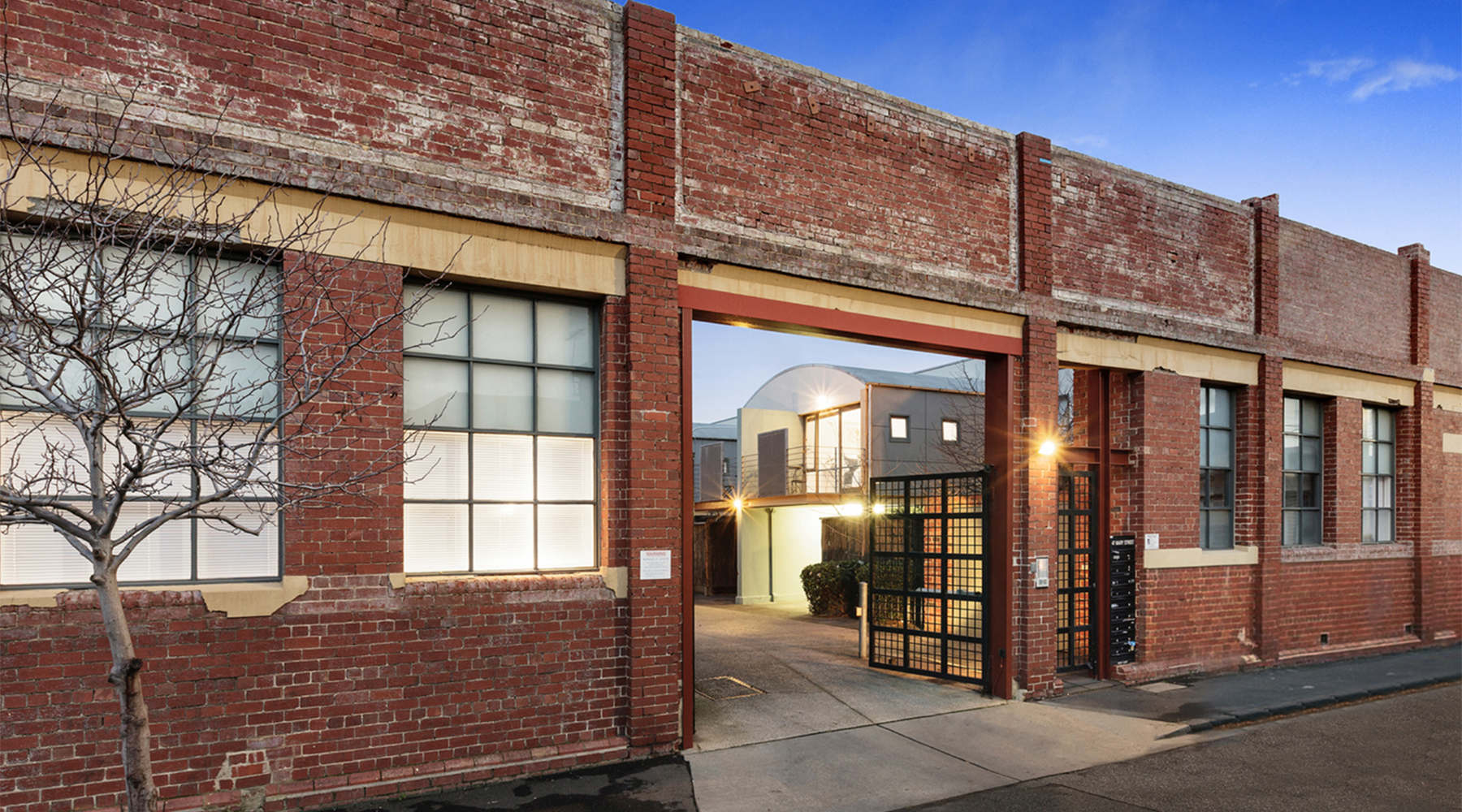 Heritage warehouse façade illuminated at dusk with secure gated entry to the private residential courtyard.