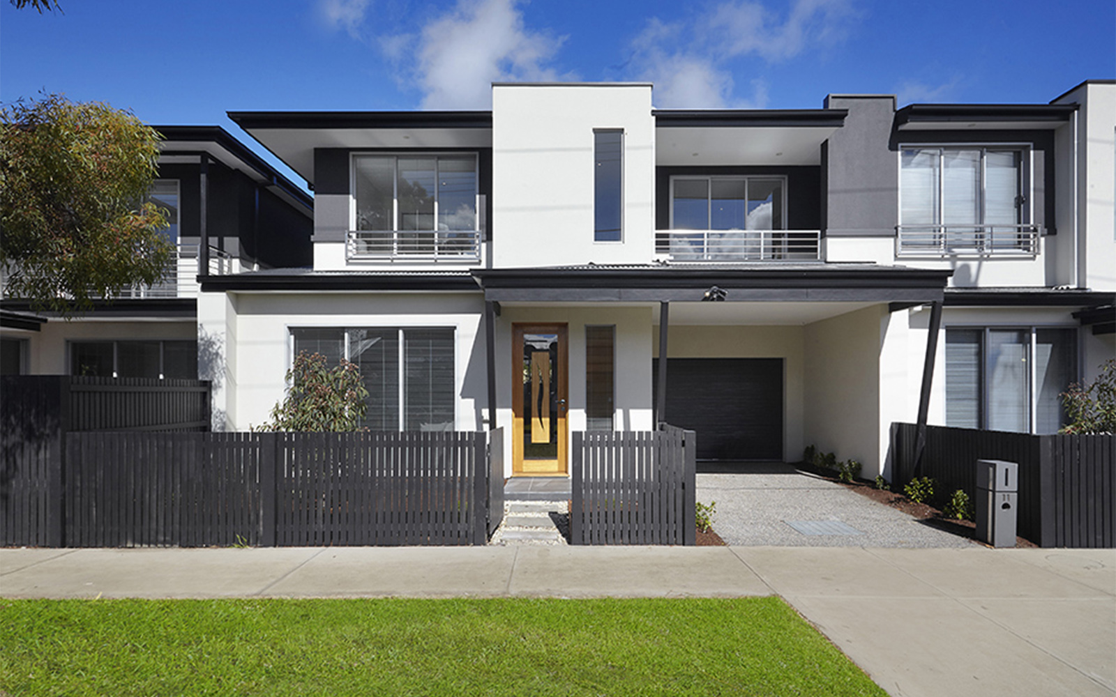 Front elevation of a two-storey townhouse with a fenced front yard, covered entry and attached garage.