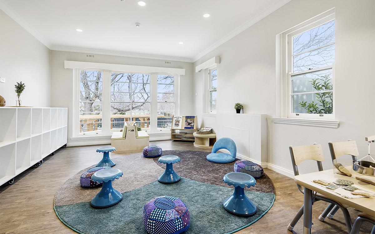 Children's learning room with low seating, activity tables, shelving and large windows overlooking an outdoor area.
