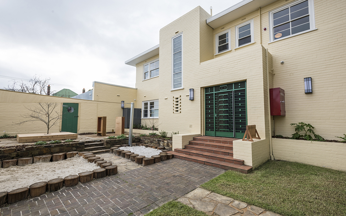 Courtyard entrance with landscaped play area, paved pathways and two-storey childcare building.