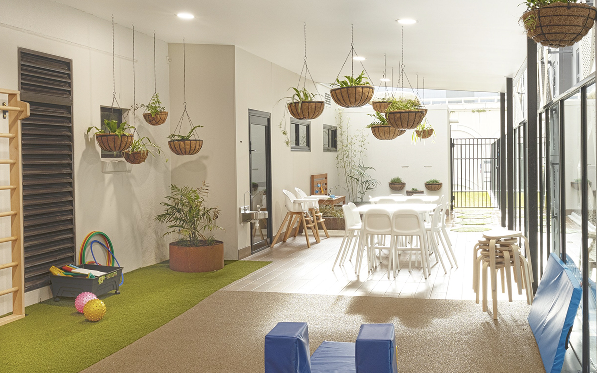 Indoor-outdoor learning space at HEI Schools with hanging plants, play equipment and children's activity tables.