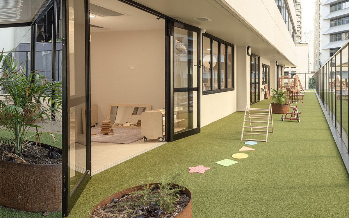 Outdoor learning terrace at HEI Schools with artificial turf, play equipment and direct classroom access.
