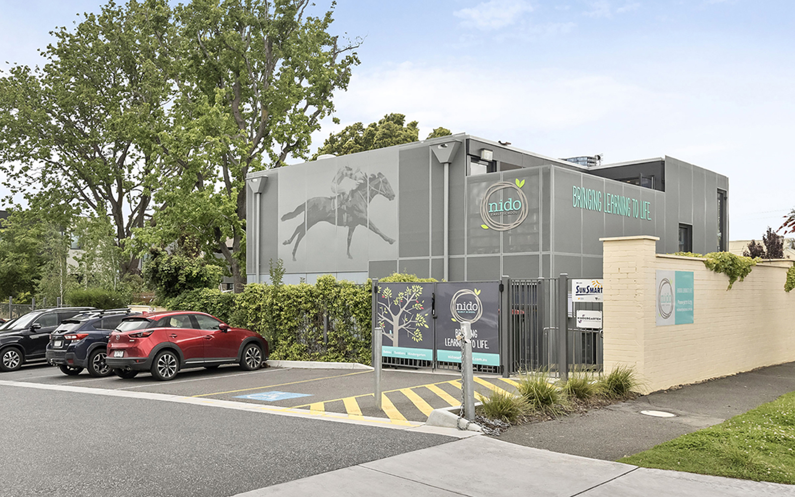 Street view of the childcare centre entrance with parking area, signage and surrounding landscaping.