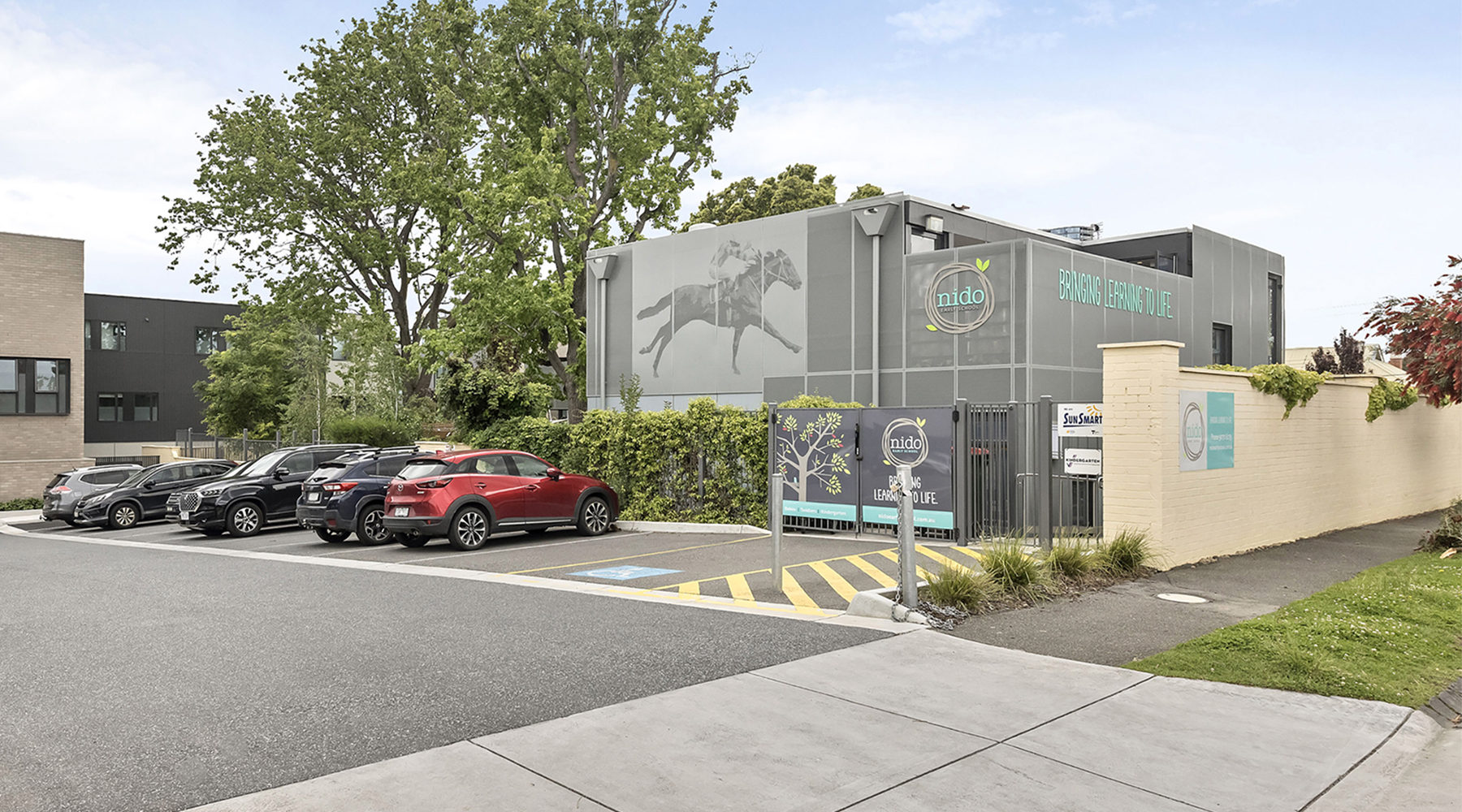 Street view of the childcare centre with entry signage, parking spaces and landscaped frontage.