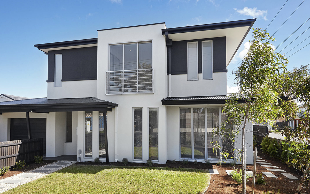 Rear view of a two-storey townhouse with lawn, landscaped garden and large ground-floor windows.