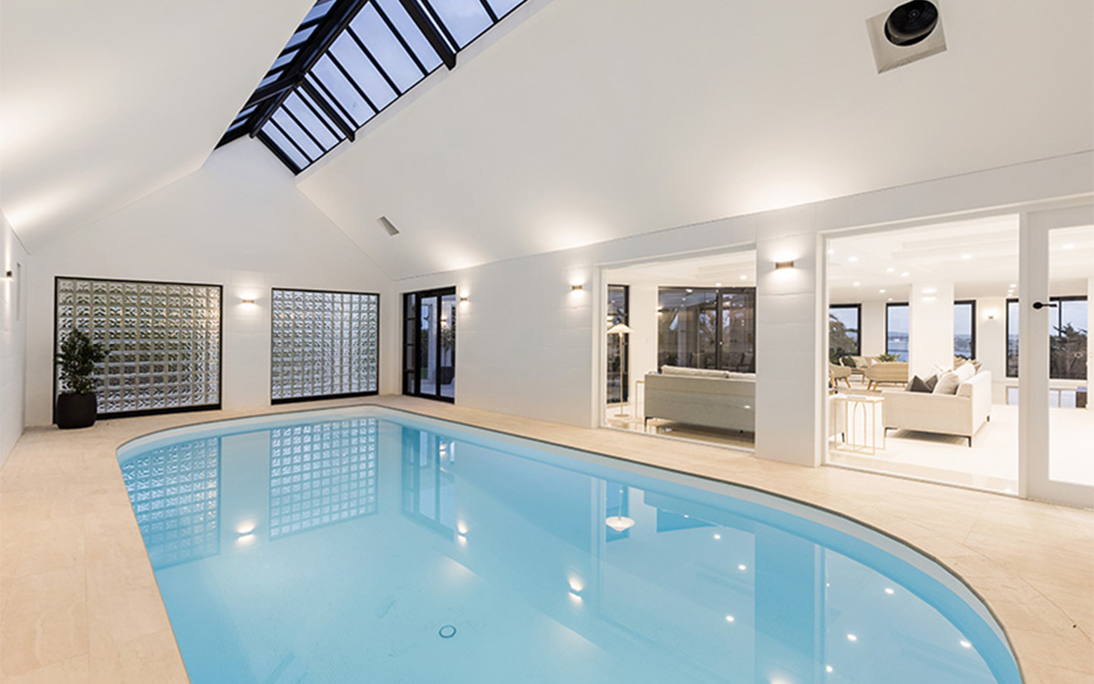 Indoor swimming pool with skylights and adjoining open-plan living spaces.
