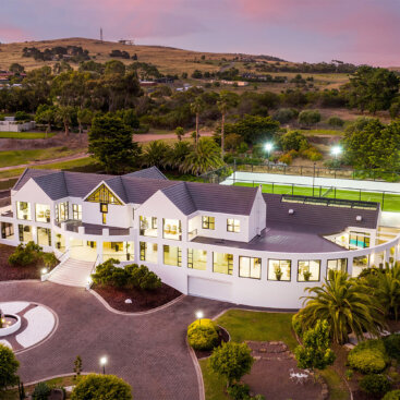 Aerial twilight view of the luxury residence showcasing landscaped grounds, tennis court and surrounding countryside.