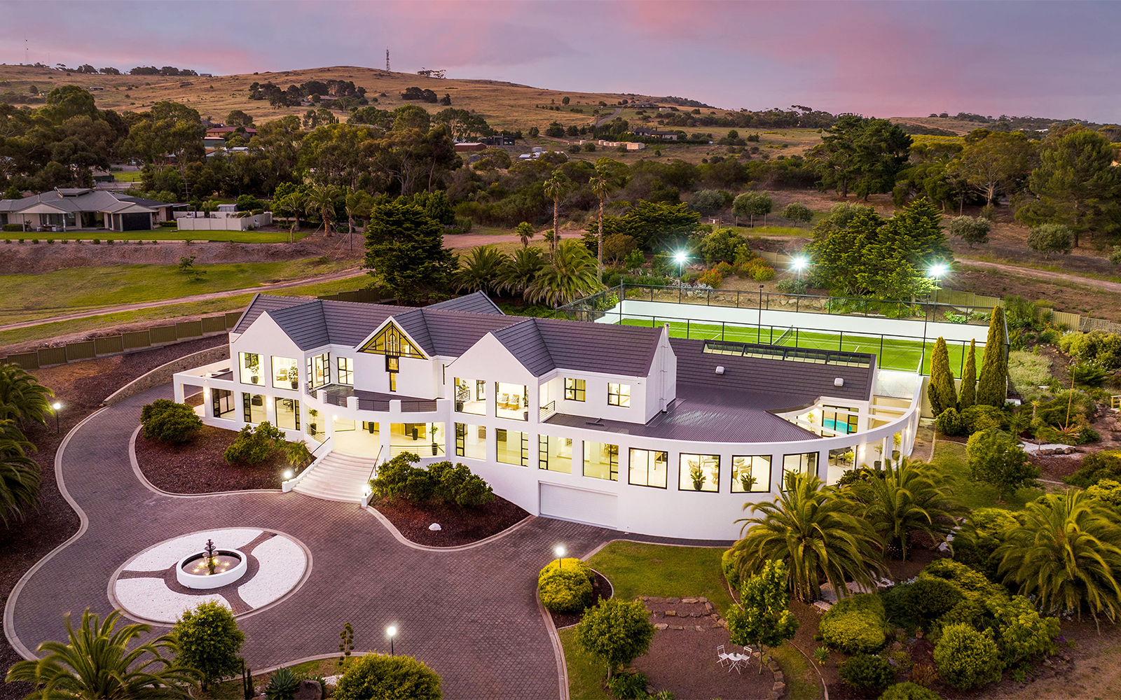 Aerial twilight view of the luxury residence showcasing landscaped grounds, tennis court and surrounding countryside.