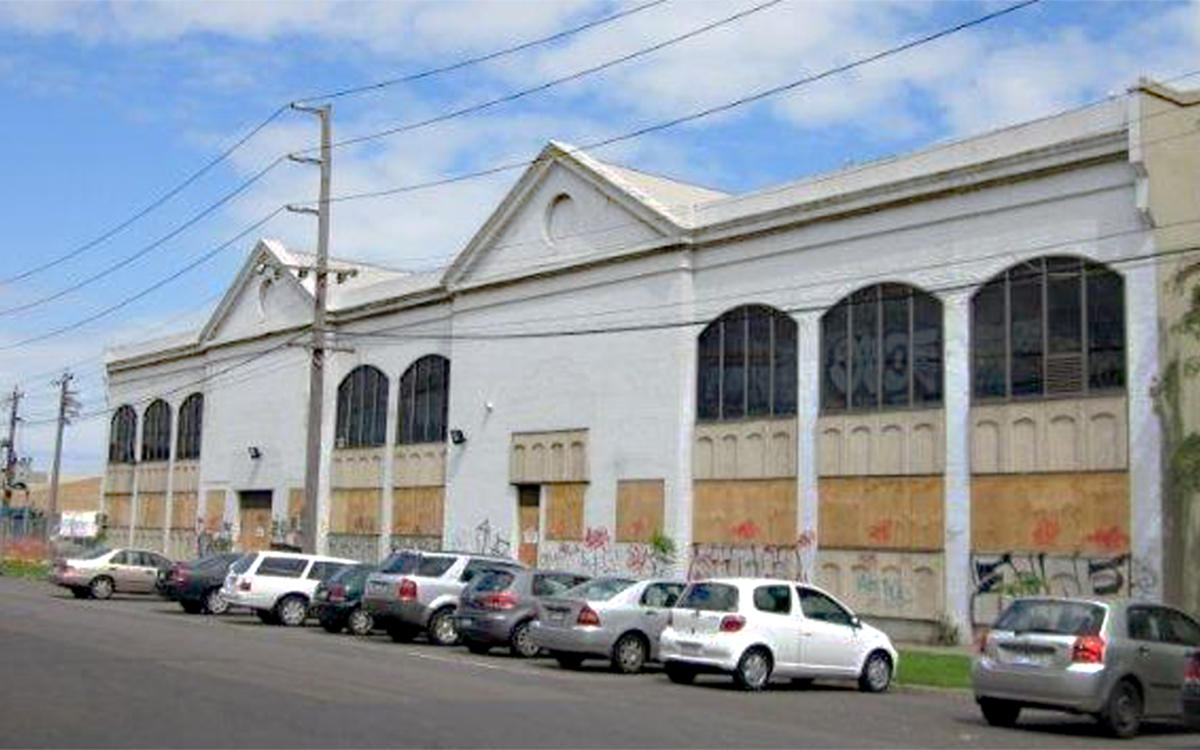 Existing commercial building with arched windows, boarded openings and street parking in South Melbourne.