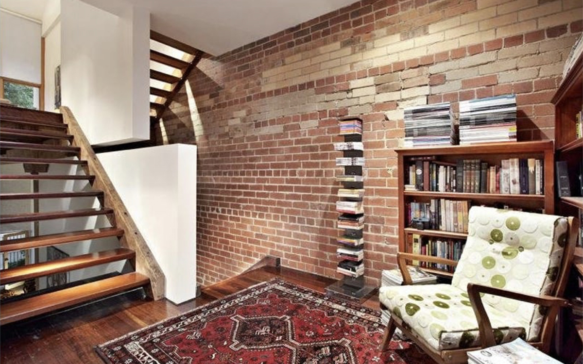 Reading nook with exposed brick wall, open staircase, bookshelves and seating area at Tullo Place.