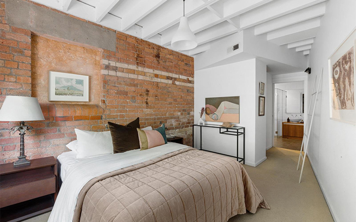Bedroom with exposed brick feature wall, high ceiling and ensuite access at Tullo Place.